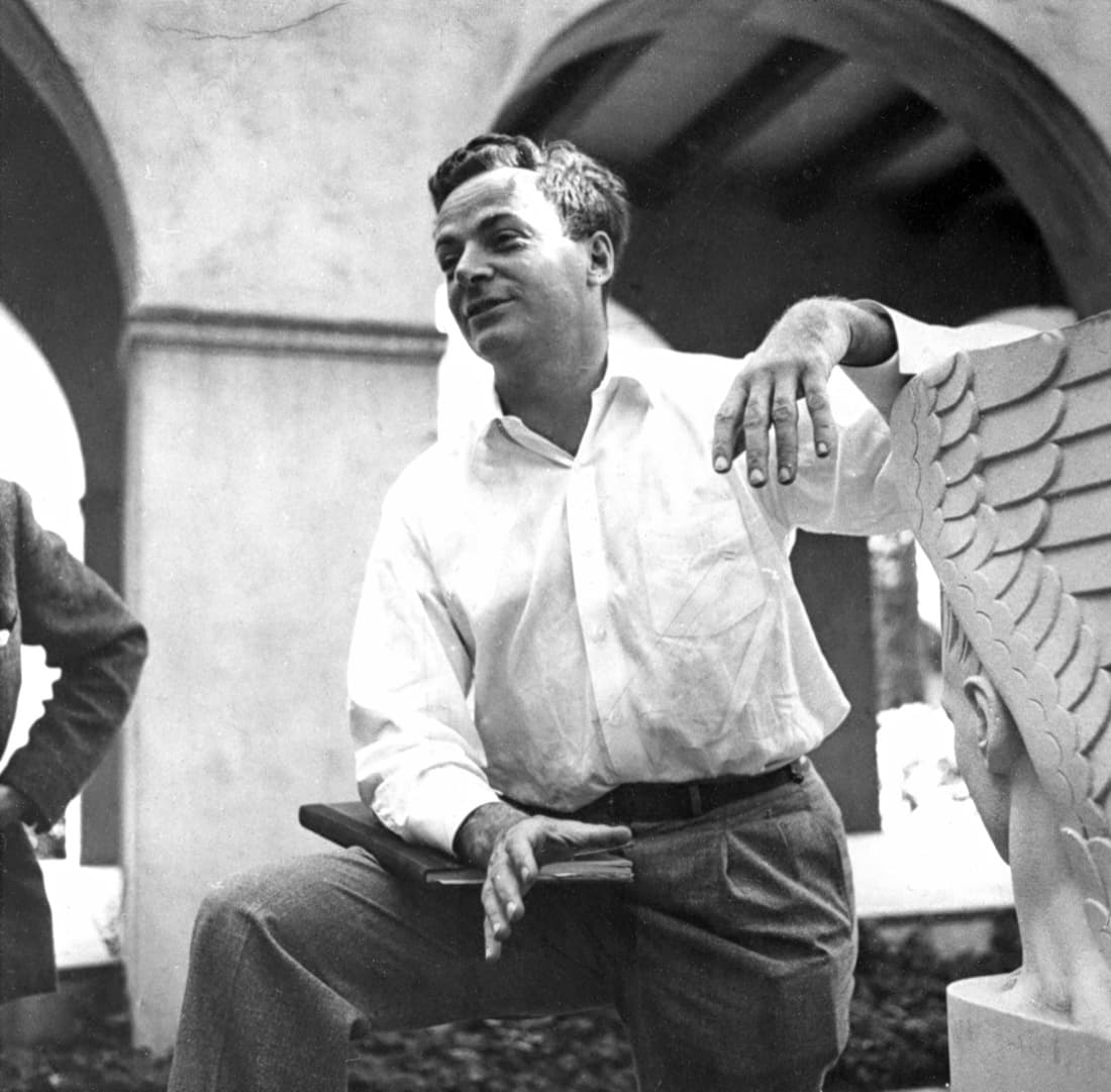 Richard Feynman sitting beside a winged sculpture at Caltech